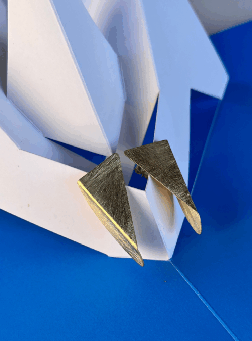 Orecchini geometrici origami metallico in lamina di ottone artigianali con rifinitura in oro chiaro satinato con piega e forma asimmetrica che cambia con il movimento della testa. Gioielli ispirati alle sculture da viaggio di Bruno Munari