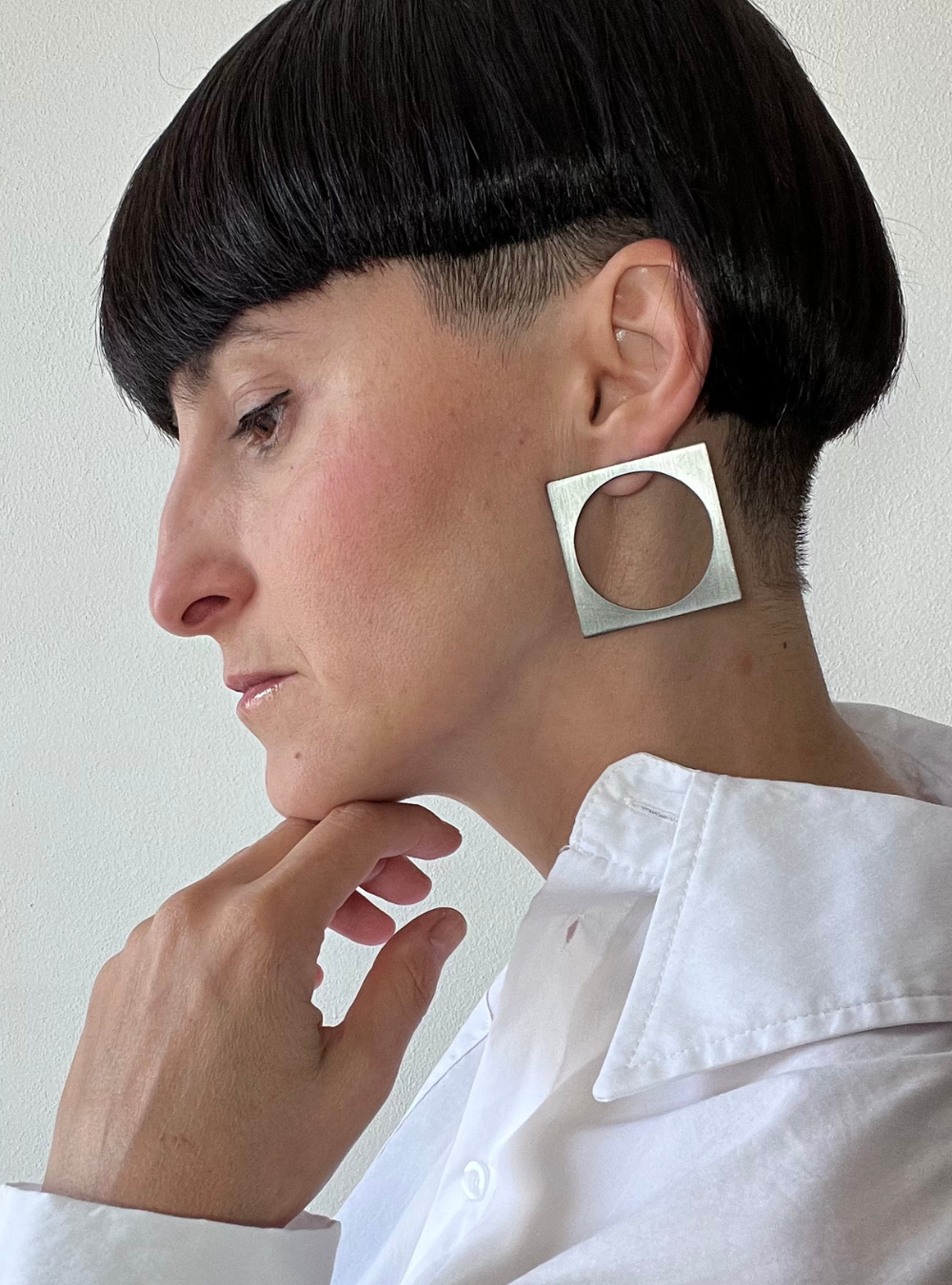 Orecchini quadrato black big a perno artigianali in ottone con finitura black satinato. La forma geometrica è minimalista, composta da un quadrato nero con un cerchio ritagliato al centro e chiusura a farfallina sul retro.
